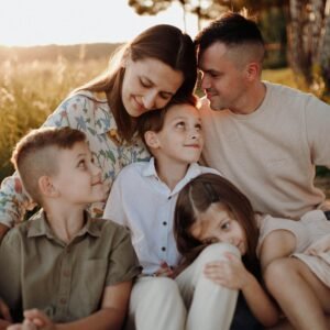 A joyful family of five sitting together, enjoying a warm sunset in the countryside.